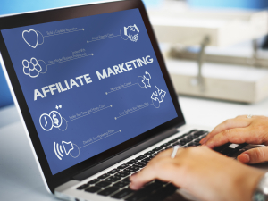 jari mengetik dengan layar background layar laptop warna biru bertulisan affiliate marketing