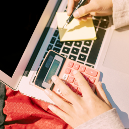 tangan perempuan di atas laptop sambil menghitung dengan kalkulator