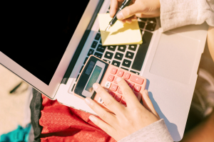 tangan perempuan di atas laptop sambil menghitung dengan kalkulator