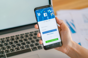 tangan memegang hp dengan layar menampilkan facebook ads
